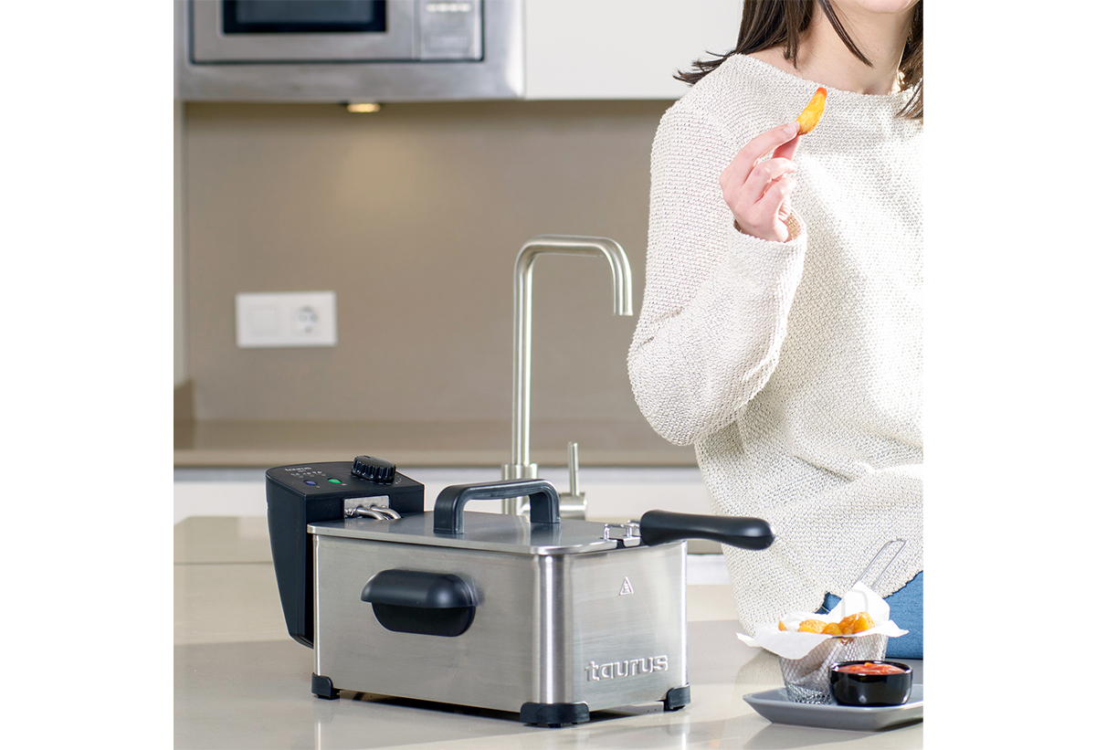 Απεικονίζεται η φριτέζα. Δίπλα μια γυναίκα και ένα δοχείο με τηγανητές πατάτες και σος.